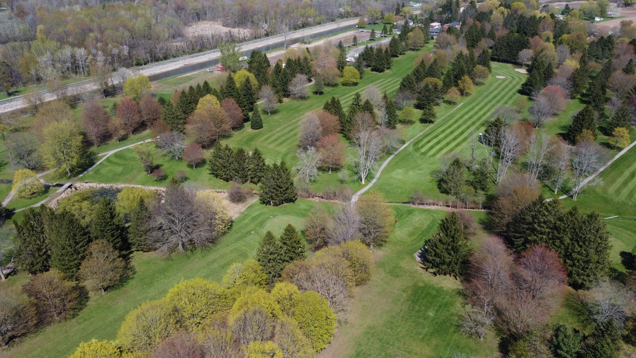 golf course with green grass and trees. A road runs alongside the course.